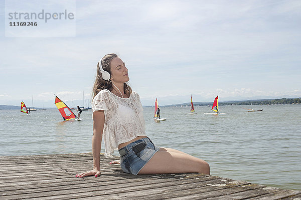 Frau hört Musik und sitzt auf der Uferpromenade am See  Ammersee  Oberbayern  Deutschland