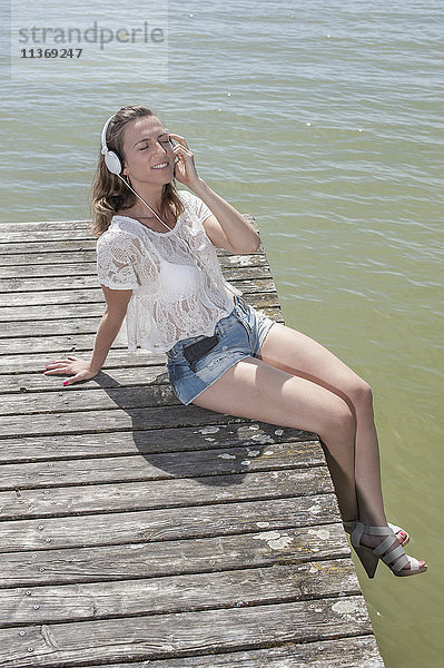 Frau hört Musik und sitzt auf der Uferpromenade am See  Ammersee  Oberbayern  Deutschland