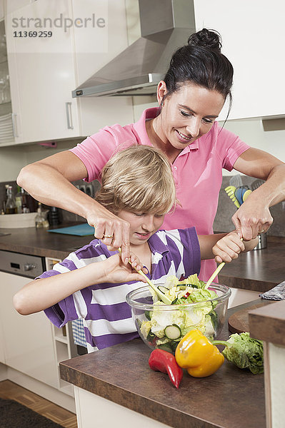 Frau mit ihrem Sohn bei der Zubereitung von Salat in der Küche