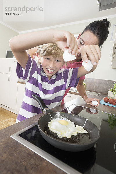 Frau mit ihrem Sohn bei der Zubereitung von Spiegeleiern in der Küche