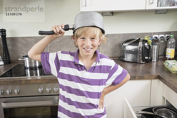 Glücklicher Junge mit Pfanne auf dem Kopf in der Küche