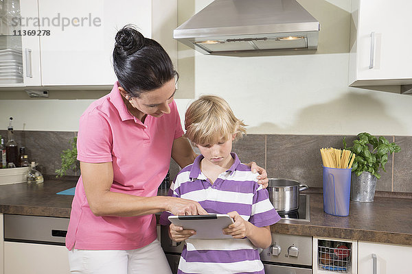 Frau mit ihrem Sohn bei der Nutzung eines digitalen Tablets in der Küche