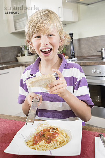 Porträt eines glücklichen Jungen  der Käse über Spaghetti reibt