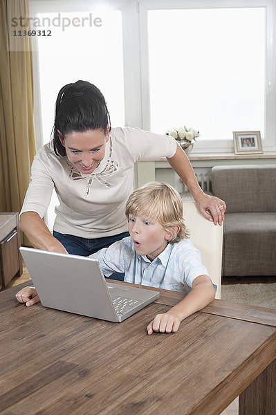 Frau mit ihrem Sohn  der einen Laptop im Wohnzimmer benutzt