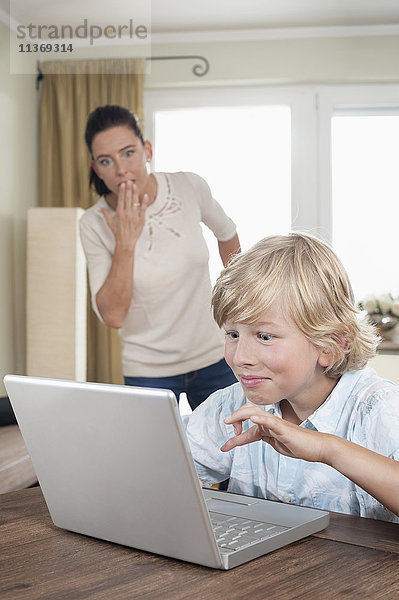 Schockierte Frau beobachtet ihren Sohn bei der Benutzung eines Laptops im Wohnzimmer