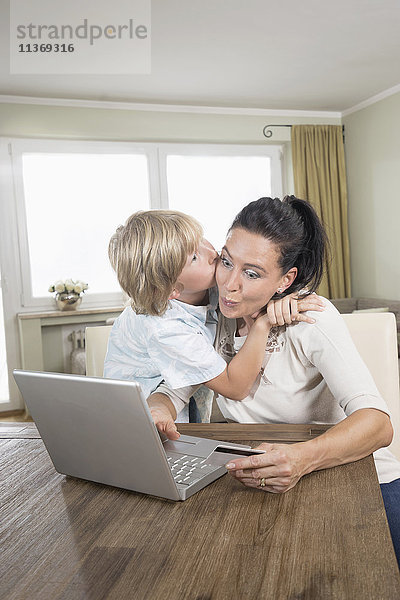 Junge küsst seine Mutter  während sie auf dem Laptop online einkauft