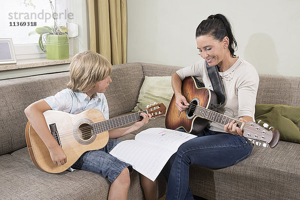 Frau mit ihrem Sohn spielt Gitarre im Wohnzimmer
