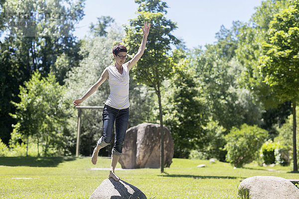 Reife Frau auf einem Bein stehend auf einem Felsen