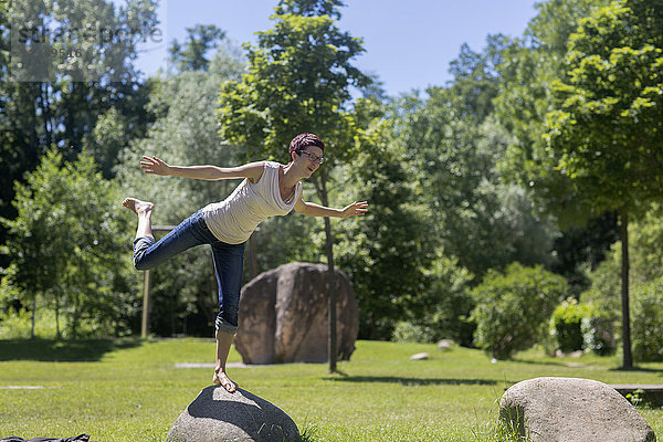 Reife Frau auf einem Bein stehend auf einem Felsen