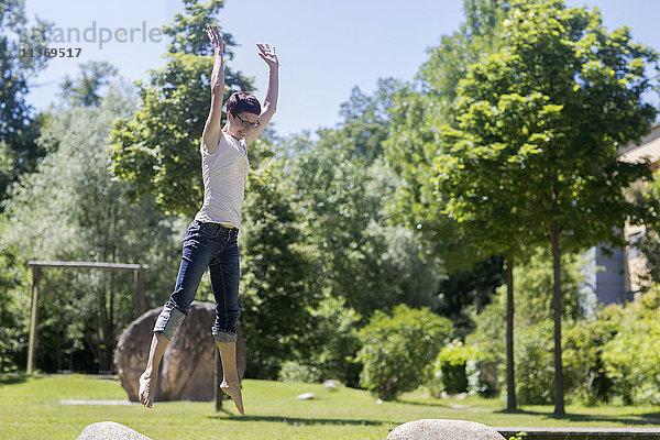 Reife Frau springt auf Felsen im Park