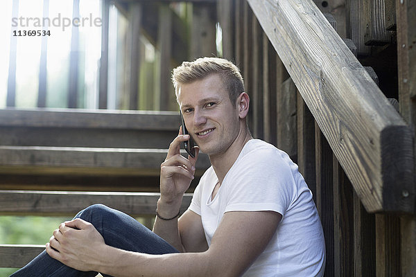 Junger Mann spricht auf einer Treppe mit seinem Handy