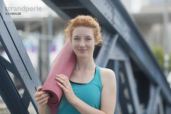 Porträt einer jungen Frau  die mit einer Gymnastikmatte in einer Stadt steht
