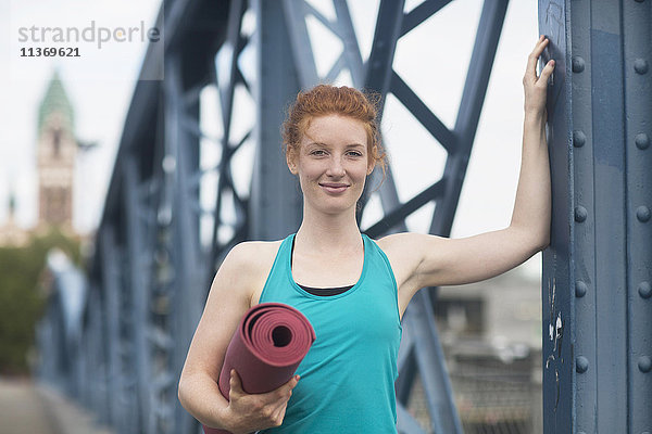 Porträt einer jungen Frau  die mit einer Gymnastikmatte in einer Stadt steht