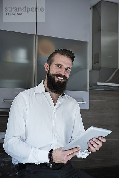 Porträt eines jungen Mannes  der ein digitales Tablet in der Küche benutzt