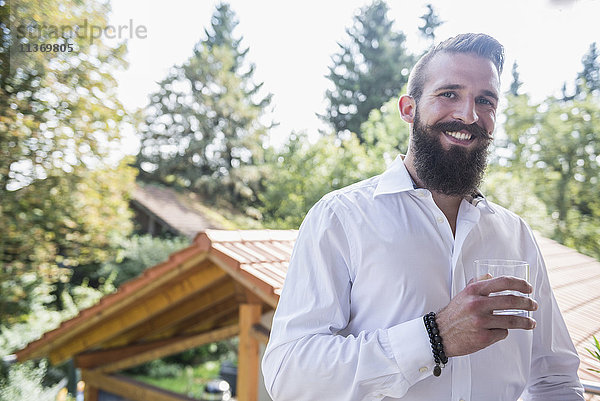 Porträt eines jungen Mannes  der auf dem Balkon Wasser trinkt und lächelt