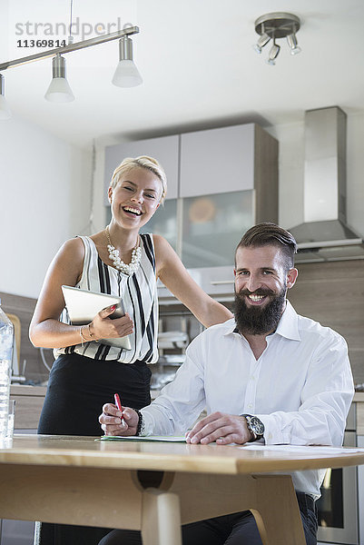 Porträt eines jungen Paares mit digitalem Tablet in der Küche und lächelnd