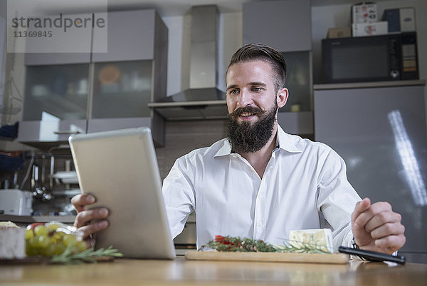 Junger Mann  der in der Küche auf einem digitalen Tablet ein Rezept für eine Mahlzeit sucht