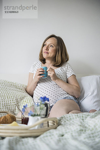 Schwangere Frau beim Frühstück im Bett