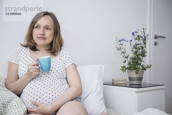 Schwangere Frau trinkt eine Tasse Kaffee im Bett