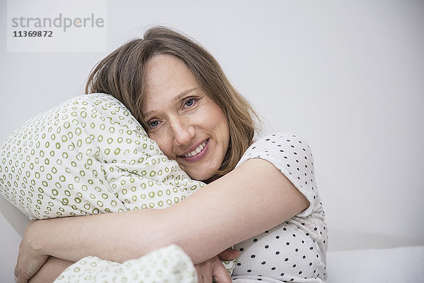 Glückliche schwangere Frau  die ihr Kissen im Bett kuschelt