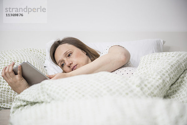 Schwangere Frau im Bett liegend und mit digitalem Tablet