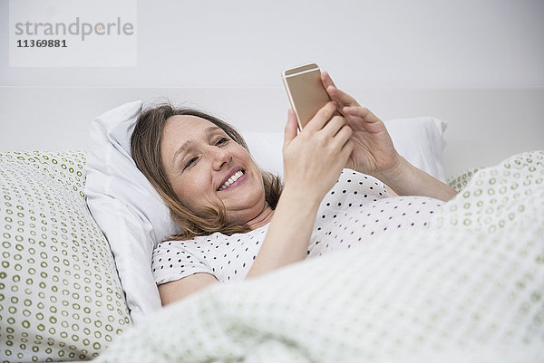 Schwangere Frau im Bett liegend und mit einem Handy telefonierend