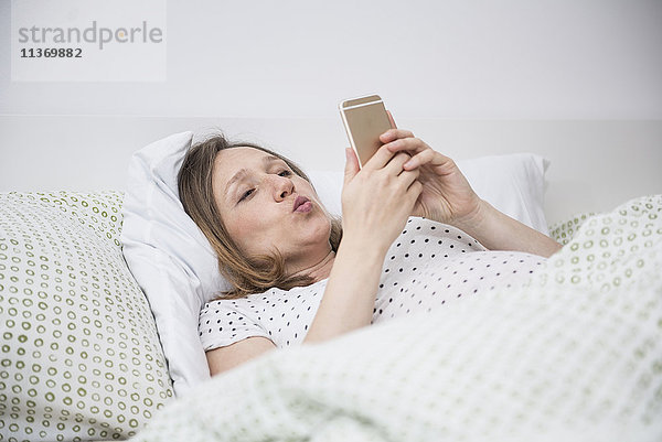 Schwangere Frau liegt im Bett und macht ein Selfie mit dem Handy