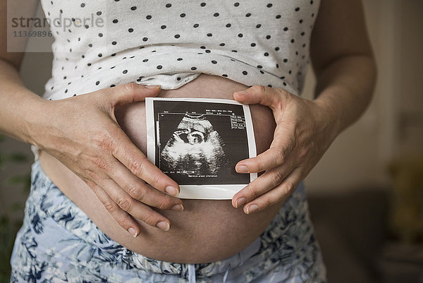 Mittelteil einer schwangeren Frau mit Ultraschallbild des Fötus