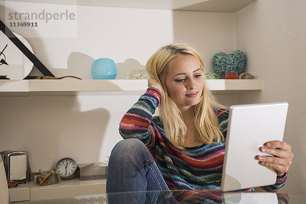 Schöne junge Frau mit digitalem Tablet im Wohnzimmer