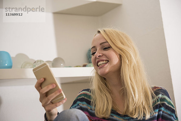 Schöne junge Frau mit Smartphone im Wohnzimmer und lächelnd