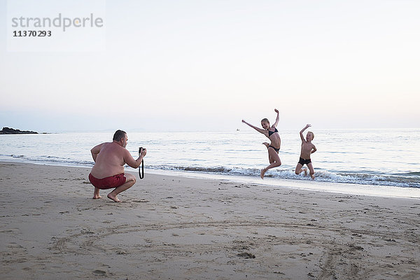 Vater fotografiert seine Kinder am Strand