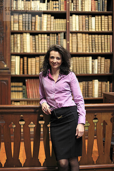 Elegante braunhaarige junge Frau in einer Bibliothek mit alten Büchern im Regal.