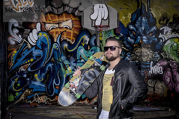 Mann mit Skateboard vor Graffiti-Wand