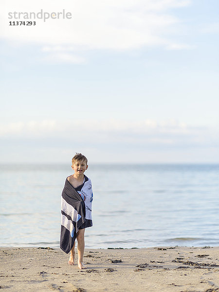 Junge in Handtuch eingewickelt am Strand
