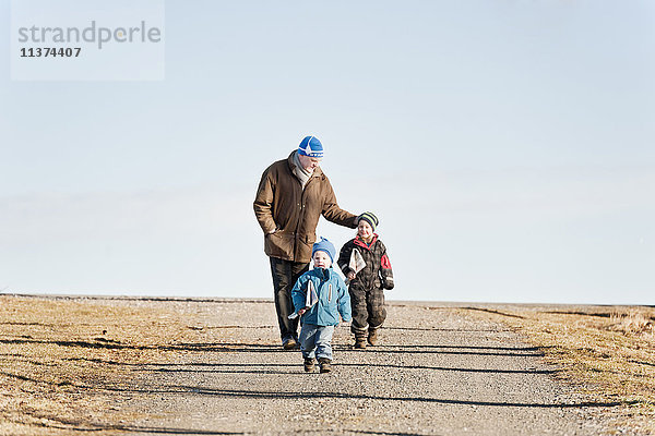 Großvater und Enkelkinder spazieren entlang einer Landstraße