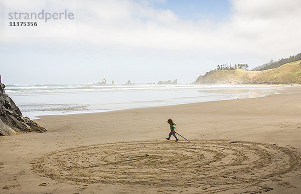 Kaukasisches Mädchen zeichnet Kreise am Strand mit einem Stock