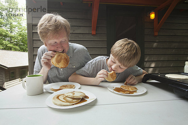Kaukasischer Vater und Sohn essen Pfannkuchen im Freien