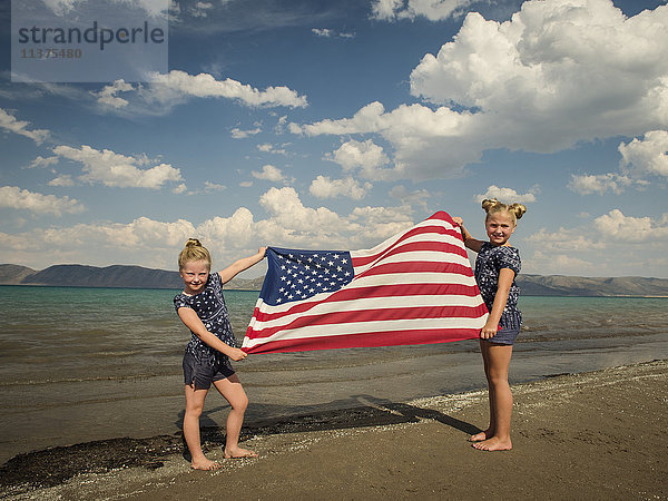 Kaukasische Mädchen halten amerikanische Flagge am Strand