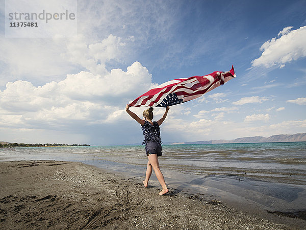 Kaukasisches Mädchen mit amerikanischer Flagge am Strand