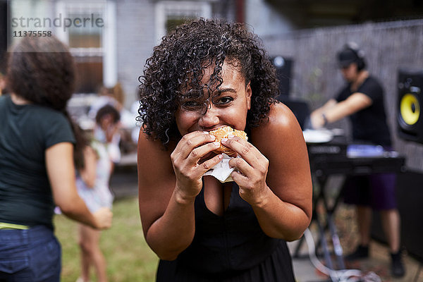 Gemischtrassige Frau isst Hamburger bei Hinterhofparty