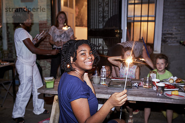 Lächelndes Mädchen  das eine brennende Wunderkerze auf einer Hinterhofparty hält