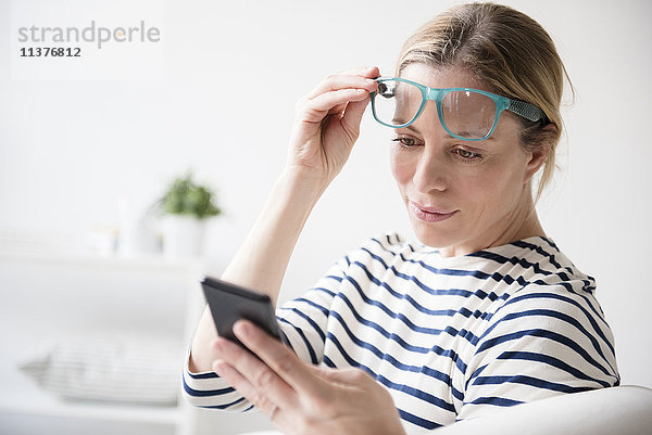 Kaukasische Frau  die eine Brille hebt und ein Mobiltelefon liest