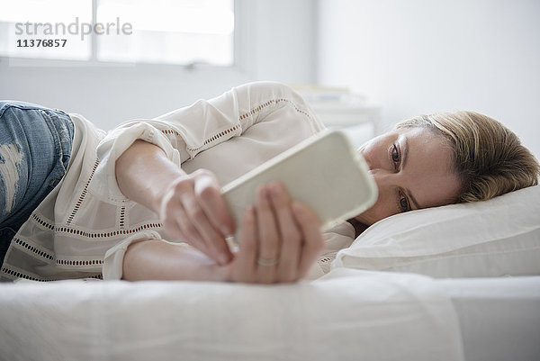Kaukasische Frau liegt auf dem Bett und schreibt eine SMS auf ihrem Handy