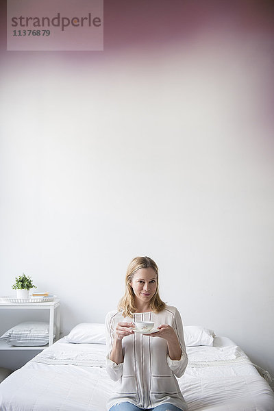 Porträt einer kaukasischen Frau  die auf einem Bett sitzt und Tee trinkt