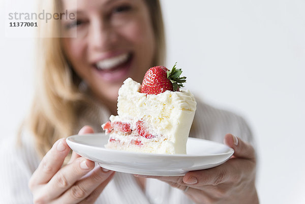 Kaukasische Frau hält ein Stück Vanillekuchen mit Erdbeere
