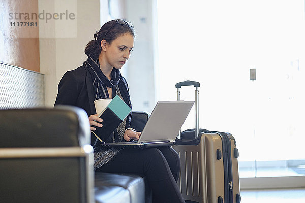 Hispanische Frau mit Reisepass und Laptop auf dem Flughafen