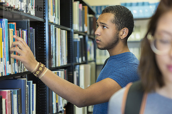 Gemischtrassiger Junge sucht sich ein Buch in der Bibliothek aus