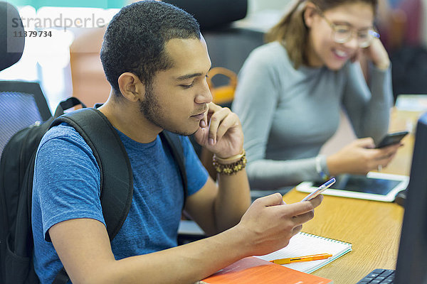 Mixed Race Junge und Mädchen texting auf Handys in der Bibliothek