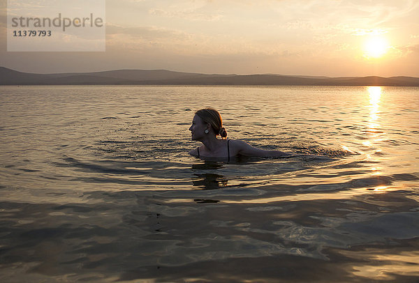 Kaukasische Frau schwimmt im See bei Sonnenuntergang