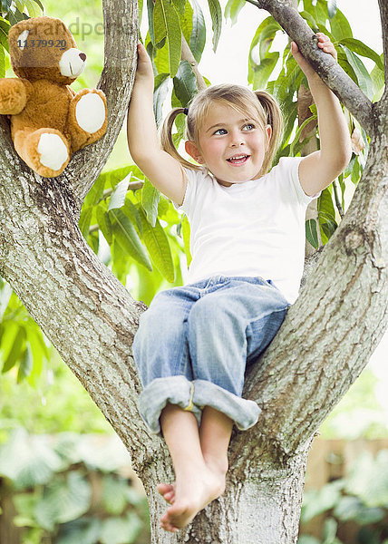 Kaukasisches Mädchen sitzt mit Teddybär im Baum